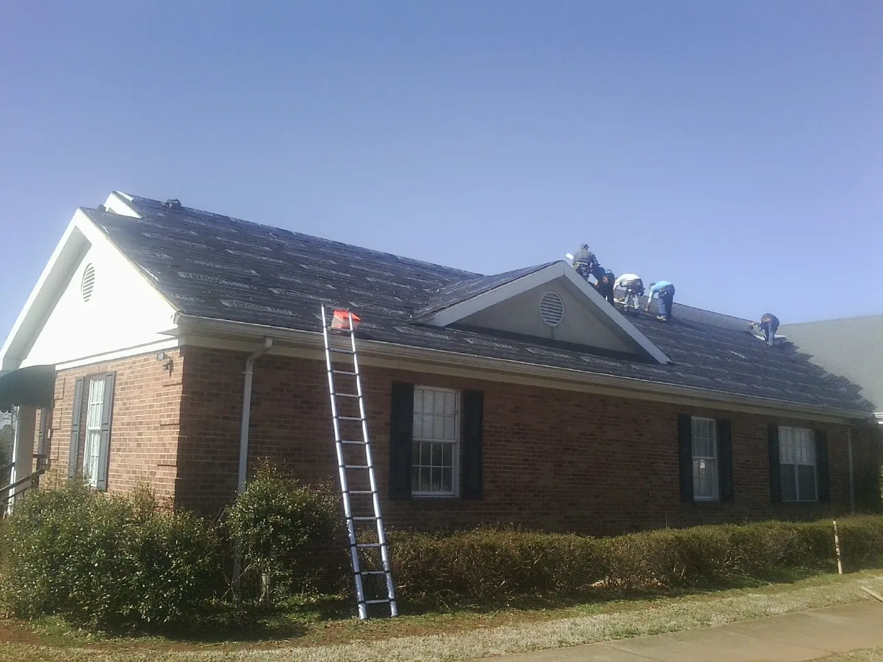 Crew tearing shingles off a brick ranch roof with a ladder set — Metal Roof Repair work by our crew in Spanish Fort
