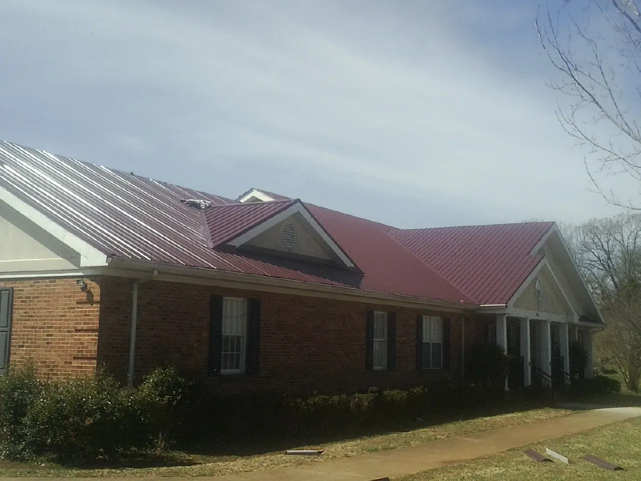 Red metal roof with gabled entries on a long brick building, from a Hail Damage Roof Repair job in Spanish Fort