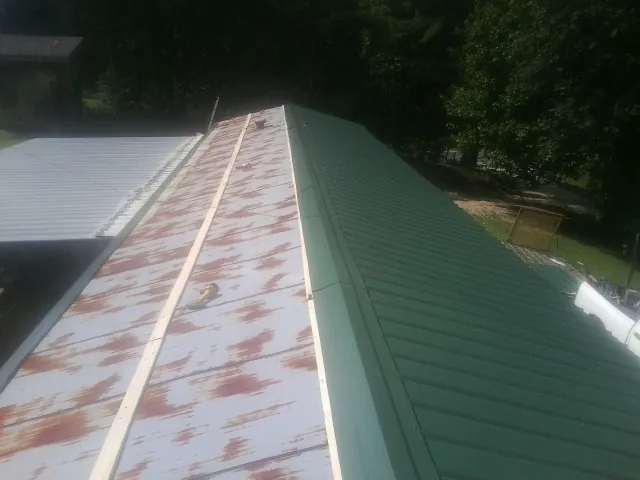 Old rusted panels beside newly installed green metal roofing — Wind Damage Roof Repair by Roofing Brothers in Spanish Fort