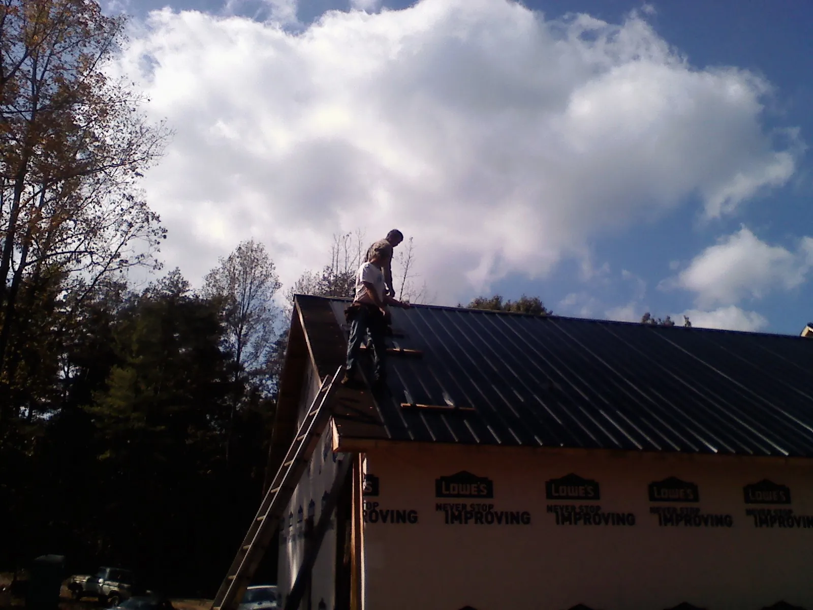 Roofer fastening dark metal panels high against a cloudy sky, from a Roof Inspection job in Spanish Fort