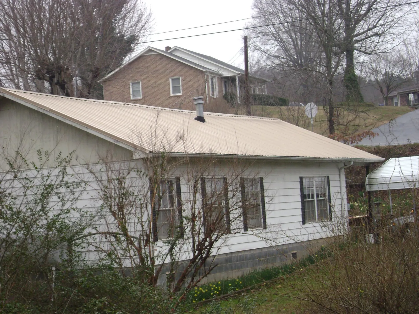 Tan metal roof on a white sided house set into a hillside — Commercial Roofing by Roofing Brothers in Spanish Fort